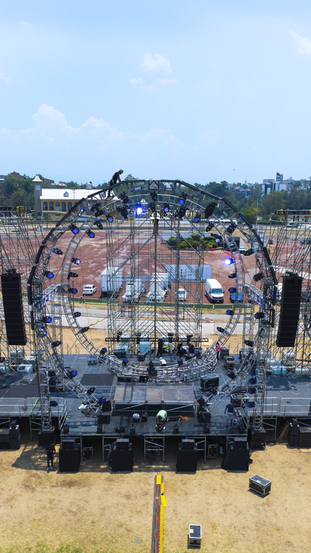 Vista lateral de unas gradas temporales con desgaste realista por uso, rodeadas de cables en el suelo de tierra y listas para recibir a los asistentes en un recinto de conciertos exterior.